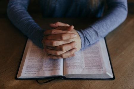 Rukoilevat kädet raamatulla kuunnellen jumalanpalvelukset netistä